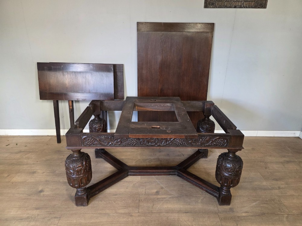 A solid dark oak extending dining table featuring carved bulbous legs, a decorative foliage apron, and a stretcher base. View XVII
