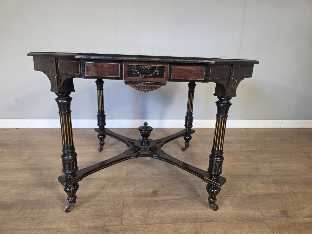 An antique Victorian octagonal centre table featuring an ebonised black finish, gilded accents, turned legs, an X-frame stretcher with a central finial, and brass castors. View VIII