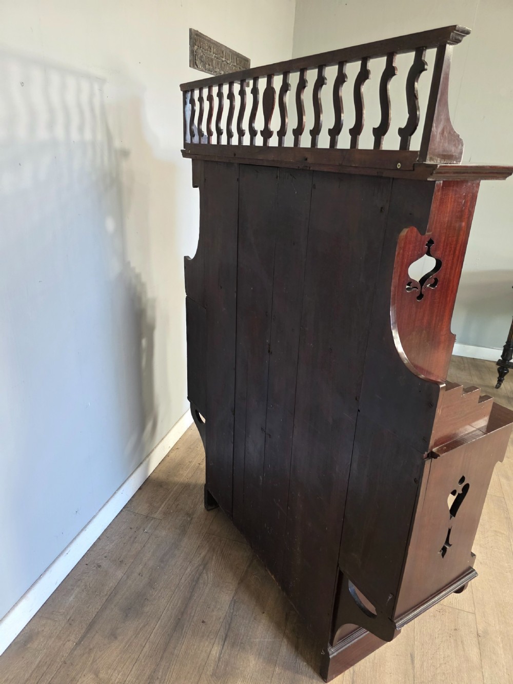 An antique dark mahogany Arts and Crafts display bookcase featuring a top galleried balustrade, open side shelves with pierced cut-outs, two glazed cabinet doors, and two middle drawers. View X