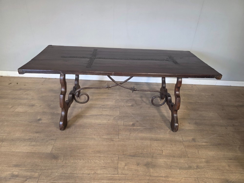 A dark brown oak refectory table featuring shaped trestle legs and a hand-forged wrought iron scrollwork stretcher beneath a rectangular top. View II