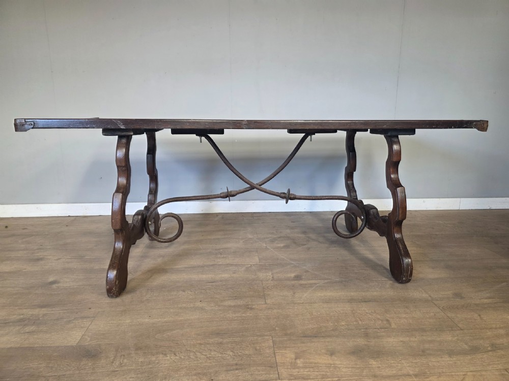 A dark brown oak refectory table featuring shaped trestle legs and a hand-forged wrought iron scrollwork stretcher beneath a rectangular top. View IV