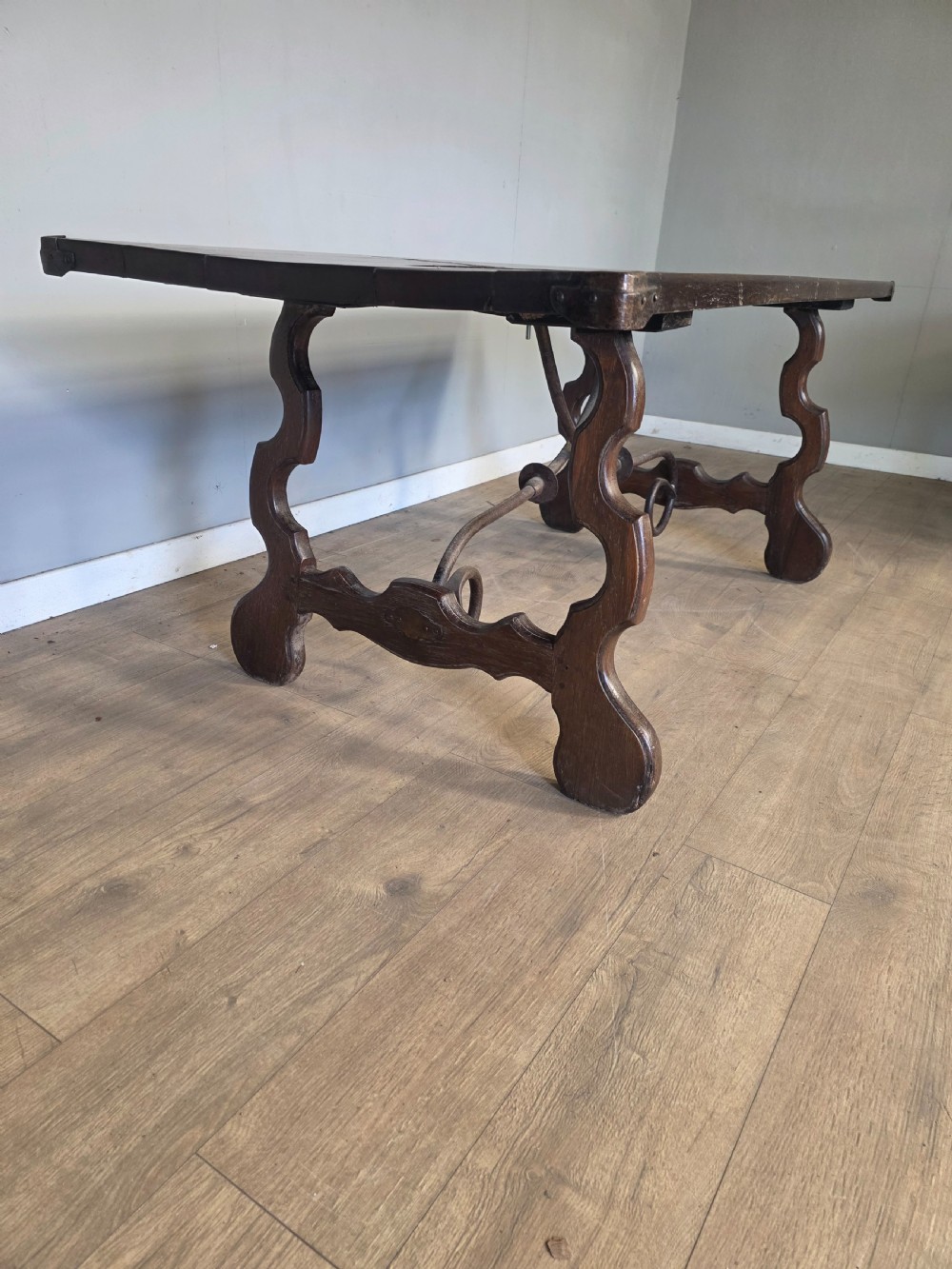 A dark brown oak refectory table featuring shaped trestle legs and a hand-forged wrought iron scrollwork stretcher beneath a rectangular top. View V