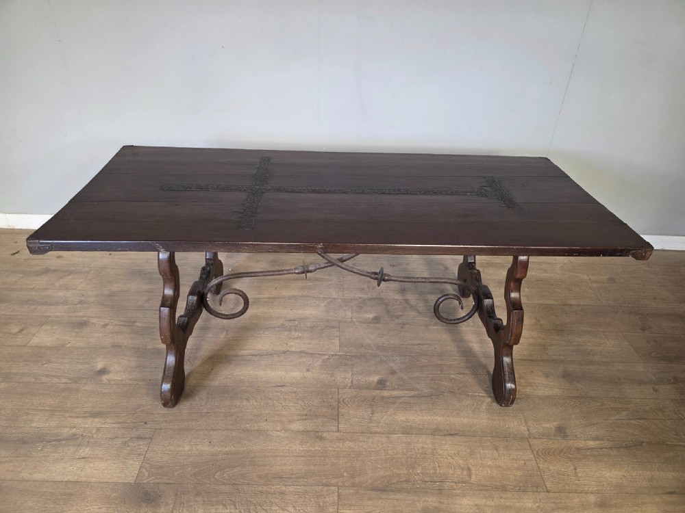 A dark brown oak refectory table featuring shaped trestle legs and a hand-forged wrought iron scrollwork stretcher beneath a rectangular top. View VI