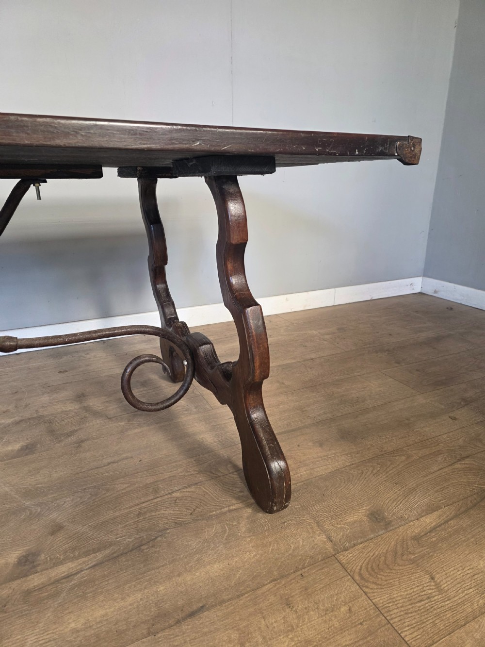 A dark brown oak refectory table featuring shaped trestle legs and a hand-forged wrought iron scrollwork stretcher beneath a rectangular top. View VIII
