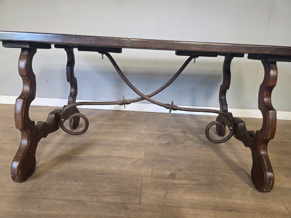 A dark brown oak refectory table featuring shaped trestle legs and a hand-forged wrought iron scrollwork stretcher beneath a rectangular top. View IX