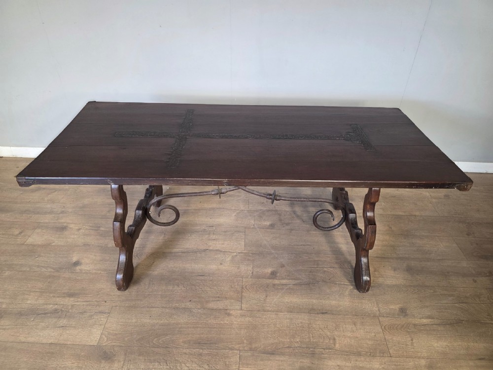 A dark brown oak refectory table featuring shaped trestle legs and a hand-forged wrought iron scrollwork stretcher beneath a rectangular top. View X