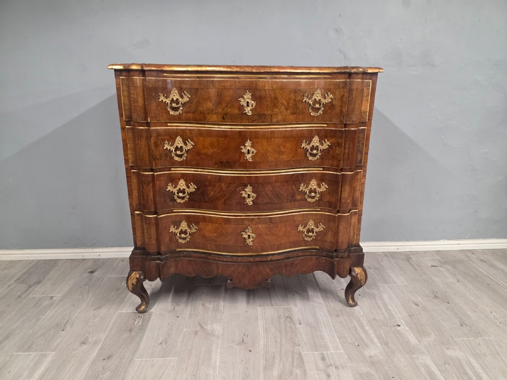 An 18th-century walnut chest of drawers featuring a serpentine front, four drawers, ornate brass handles, and short cabriole legs.