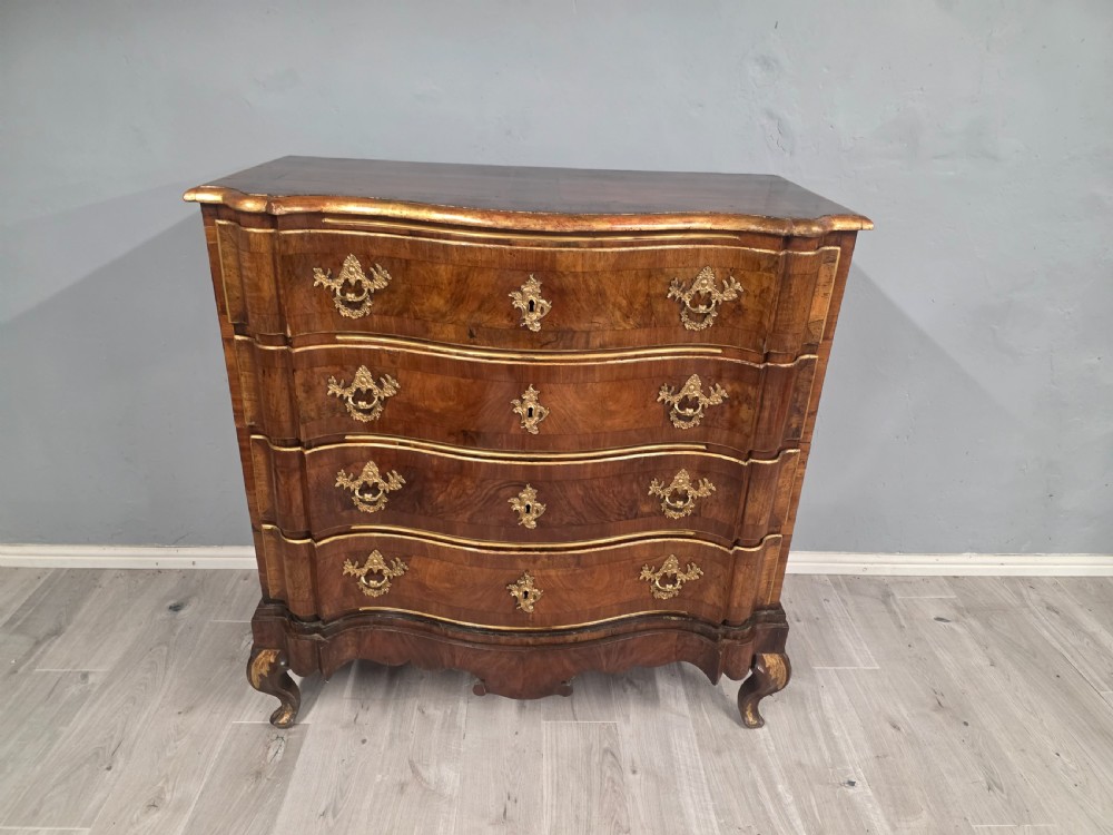 An 18th-century walnut chest of drawers featuring a serpentine front, four drawers, ornate brass handles, and short cabriole legs. View III
