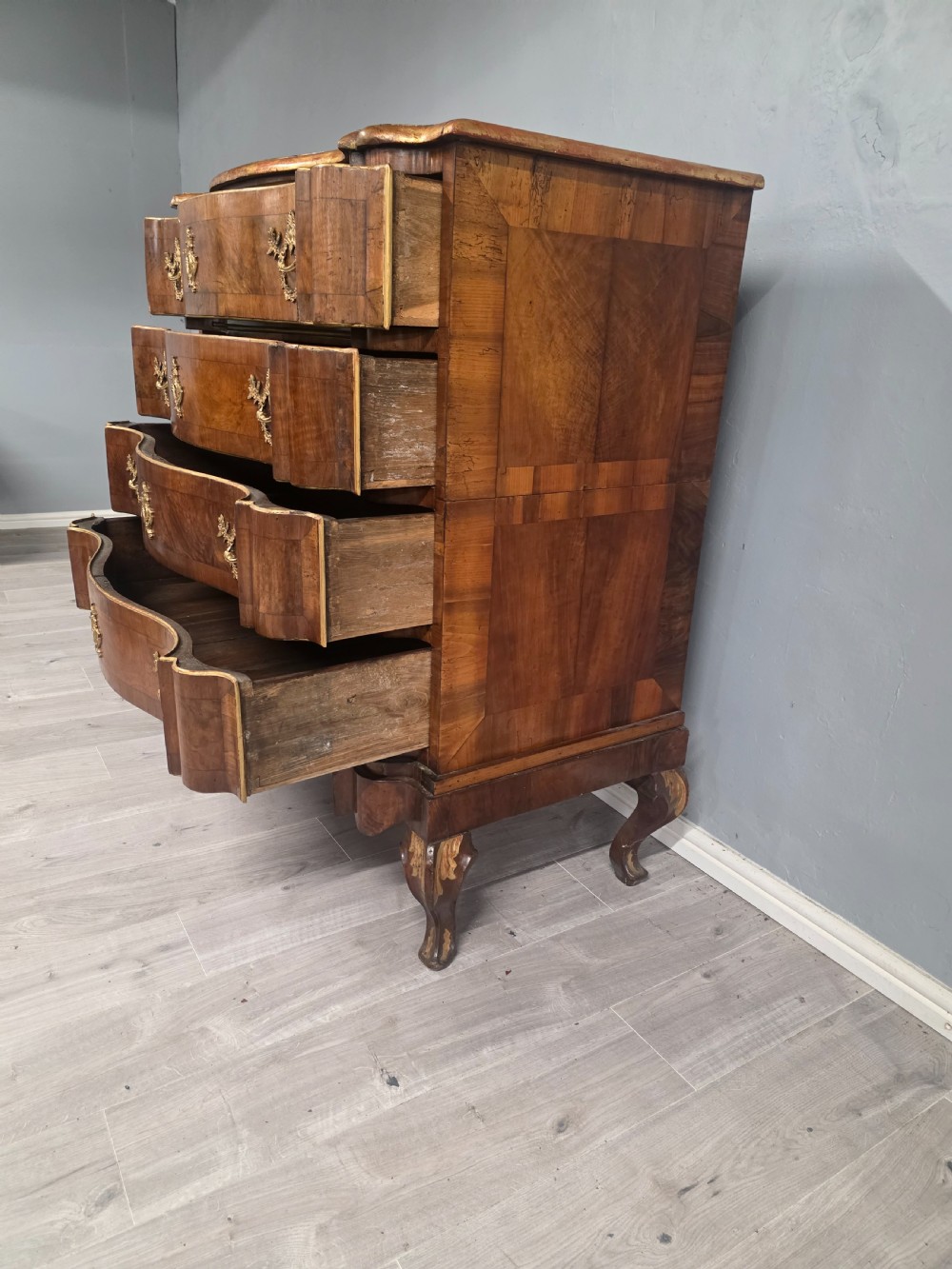 An 18th-century walnut chest of drawers featuring a serpentine front, four drawers, ornate brass handles, and short cabriole legs. View IV