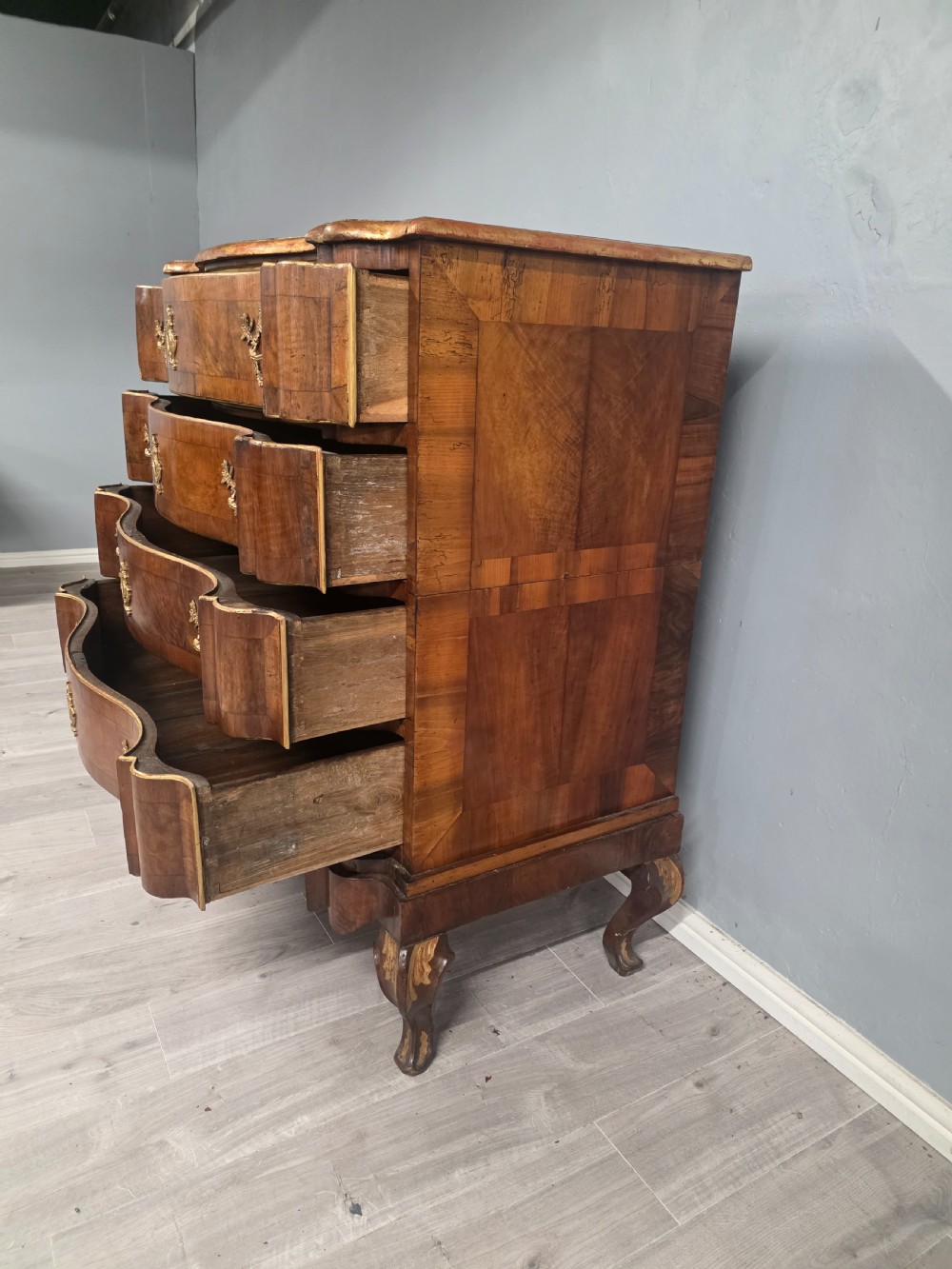 An 18th-century walnut chest of drawers featuring a serpentine front, four drawers, ornate brass handles, and short cabriole legs. View V