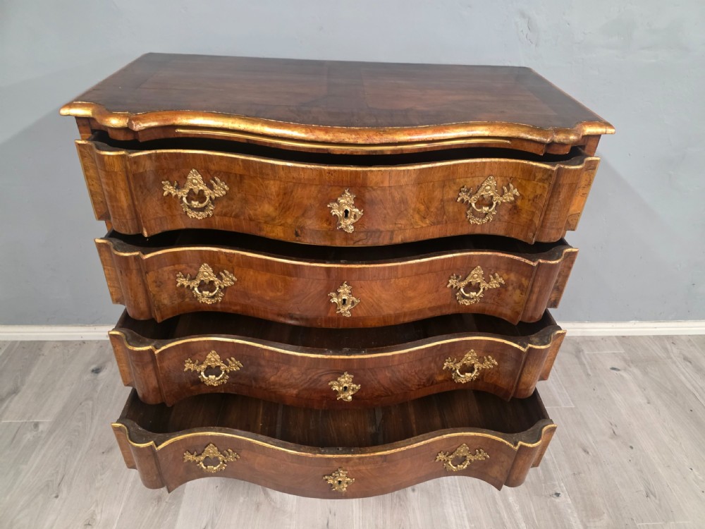 An 18th-century walnut chest of drawers featuring a serpentine front, four drawers, ornate brass handles, and short cabriole legs. View VII