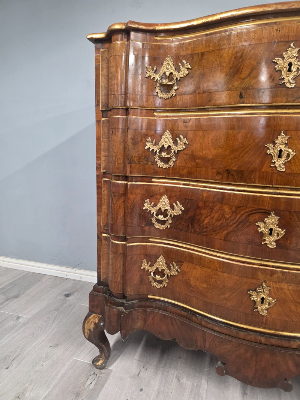 An 18th-century walnut chest of drawers featuring a serpentine front, four drawers, ornate brass handles, and short cabriole legs. View VIII