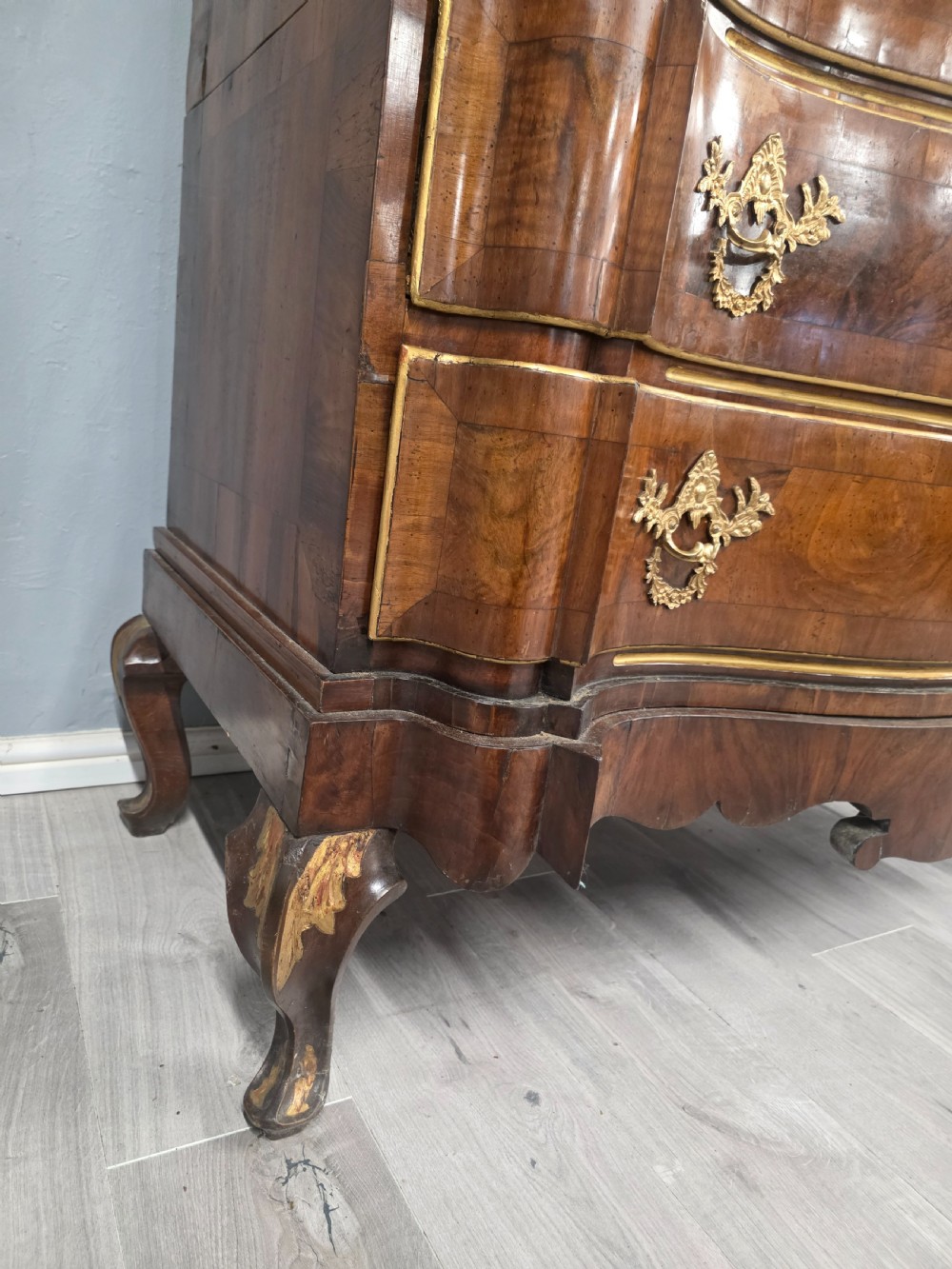 An 18th-century walnut chest of drawers featuring a serpentine front, four drawers, ornate brass handles, and short cabriole legs. View IX