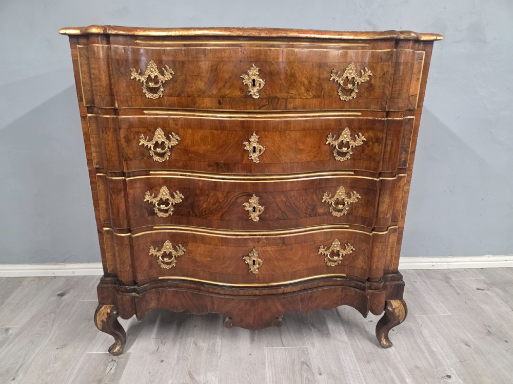 An 18th-century walnut chest of drawers featuring a serpentine front, four drawers, ornate brass handles, and short cabriole legs. View X