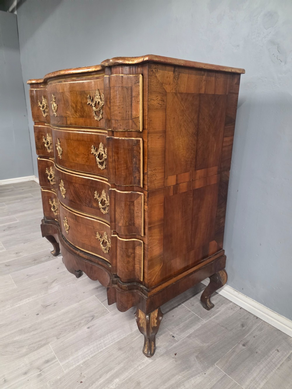 An 18th-century walnut chest of drawers featuring a serpentine front, four drawers, ornate brass handles, and short cabriole legs. View XI