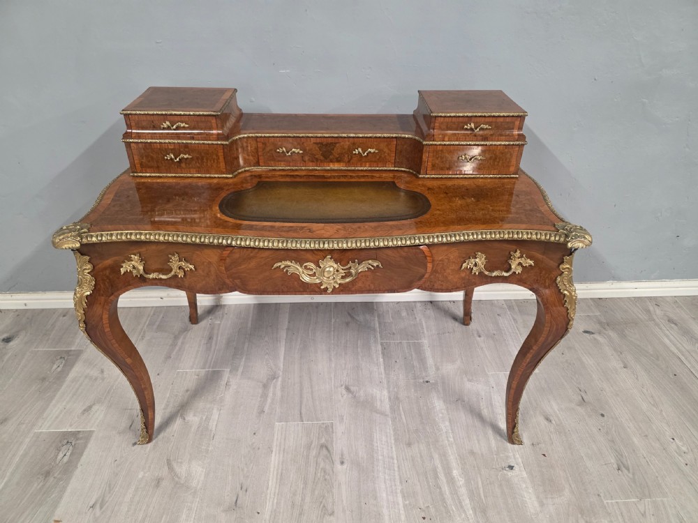 A 19th-century French Rococo Revival writing desk crafted from burr walnut with gilt-bronze mounts, a central leather writing insert, and a raised superstructure of drawers.