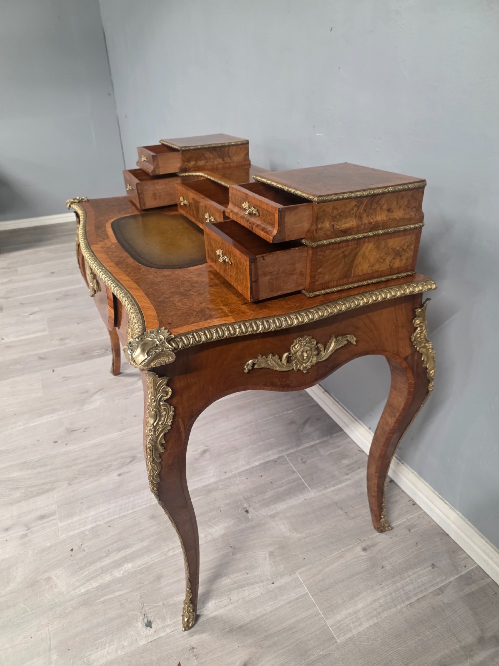 A 19th-century French Rococo Revival writing desk crafted from burr walnut with gilt-bronze mounts, a central leather writing insert, and a raised superstructure of drawers. View IV