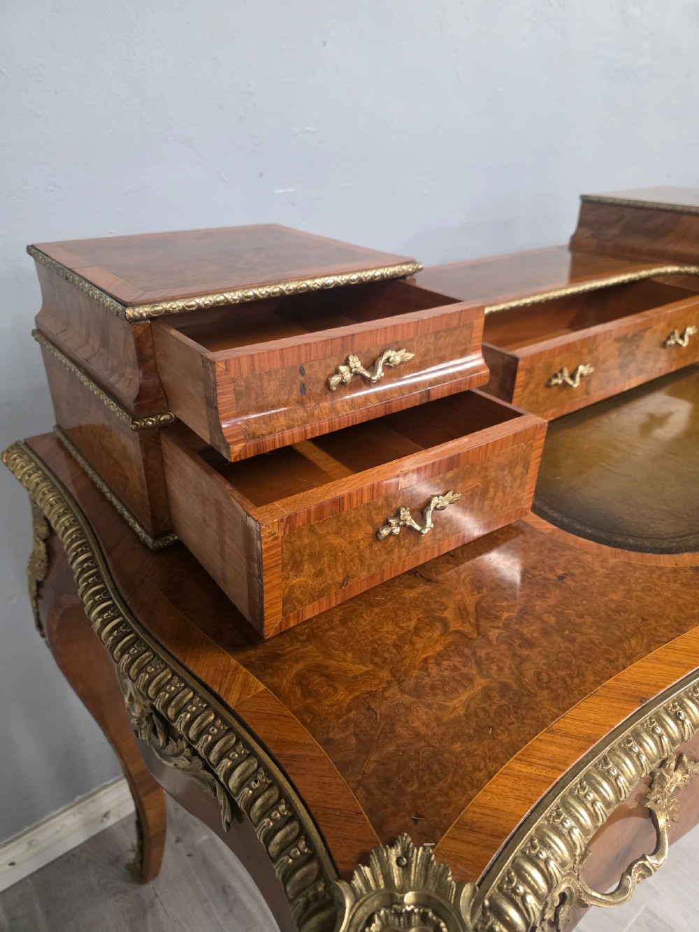 A 19th-century French Rococo Revival writing desk crafted from burr walnut with gilt-bronze mounts, a central leather writing insert, and a raised superstructure of drawers. View VI