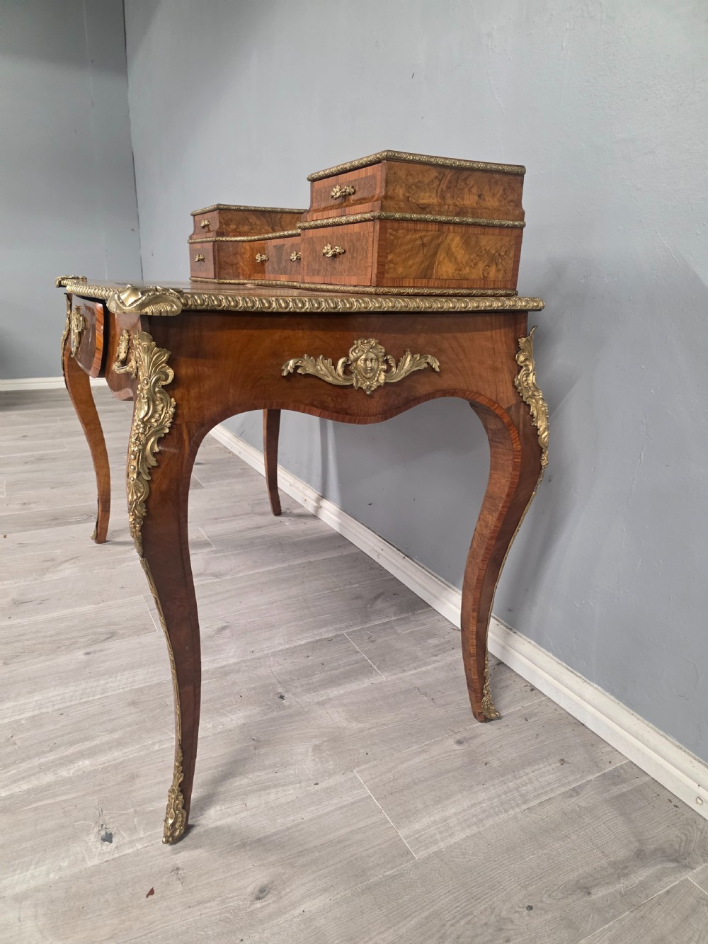 A 19th-century French Rococo Revival writing desk crafted from burr walnut with gilt-bronze mounts, a central leather writing insert, and a raised superstructure of drawers. View VIII