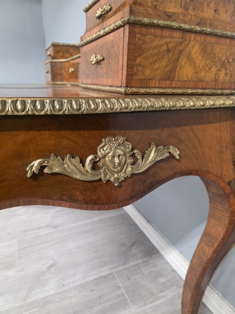 A 19th-century French Rococo Revival writing desk crafted from burr walnut with gilt-bronze mounts, a central leather writing insert, and a raised superstructure of drawers. View IX
