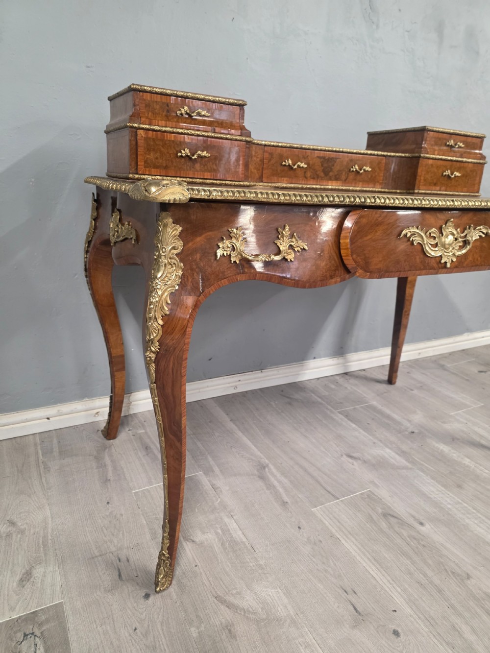 A 19th-century French Rococo Revival writing desk crafted from burr walnut with gilt-bronze mounts, a central leather writing insert, and a raised superstructure of drawers. View X