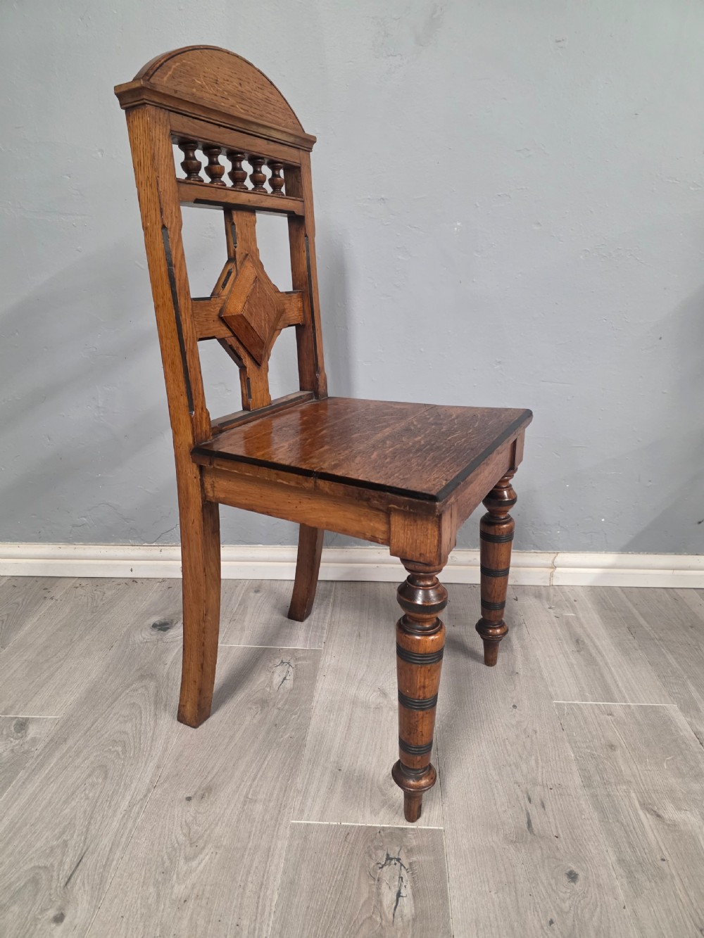 A pair of Victorian solid oak hall chairs featuring spindle pediments, central diamond back motifs, solid seats, and turned front legs. View V