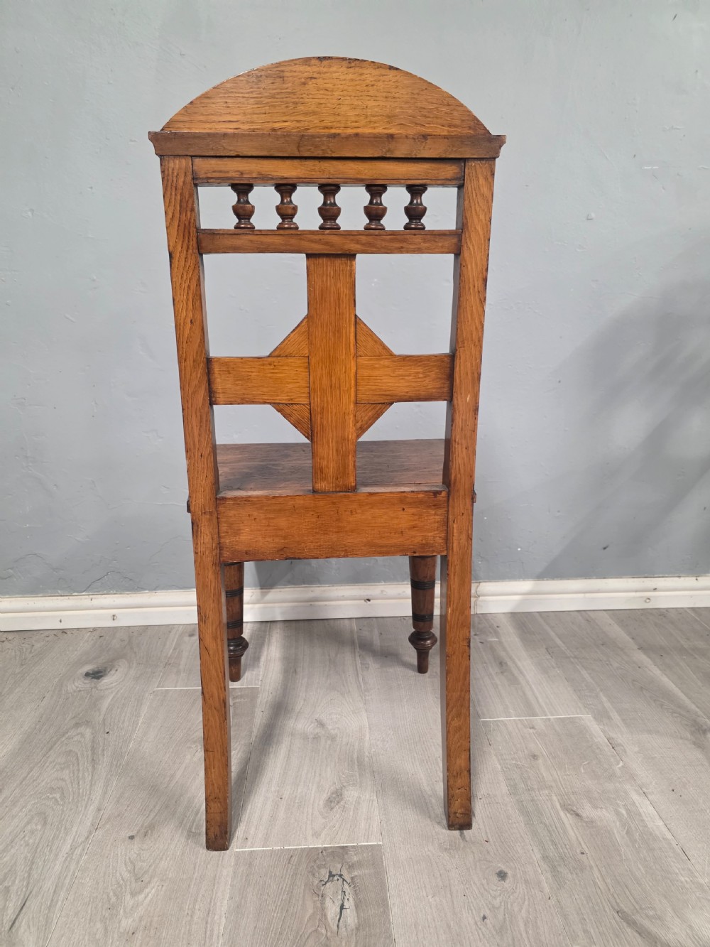 A pair of Victorian solid oak hall chairs featuring spindle pediments, central diamond back motifs, solid seats, and turned front legs. View VII