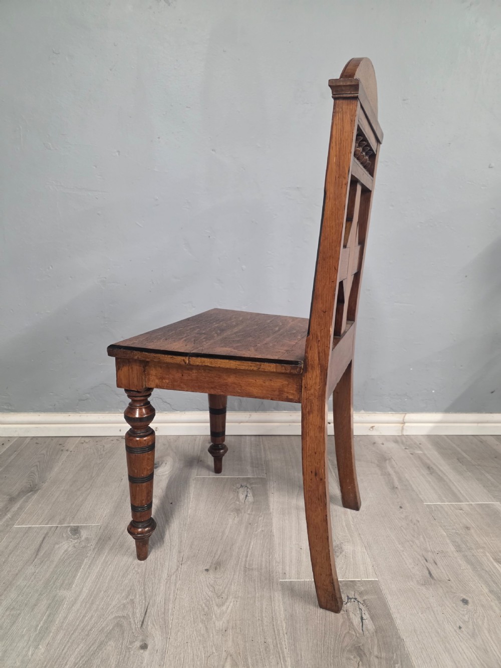 A pair of Victorian solid oak hall chairs featuring spindle pediments, central diamond back motifs, solid seats, and turned front legs. View VIII