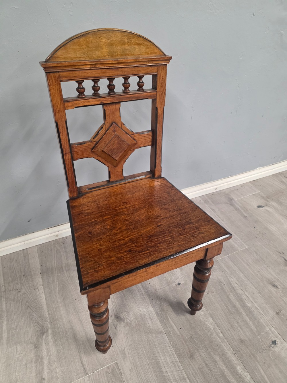 A pair of Victorian solid oak hall chairs featuring spindle pediments, central diamond back motifs, solid seats, and turned front legs. View IX