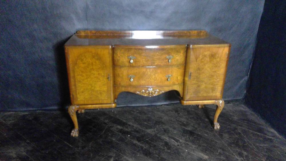 A burr walnut Queen Anne style sideboard featuring two central drawers flanked by cupboard doors, resting on carved cabriole legs with claw and ball feet.