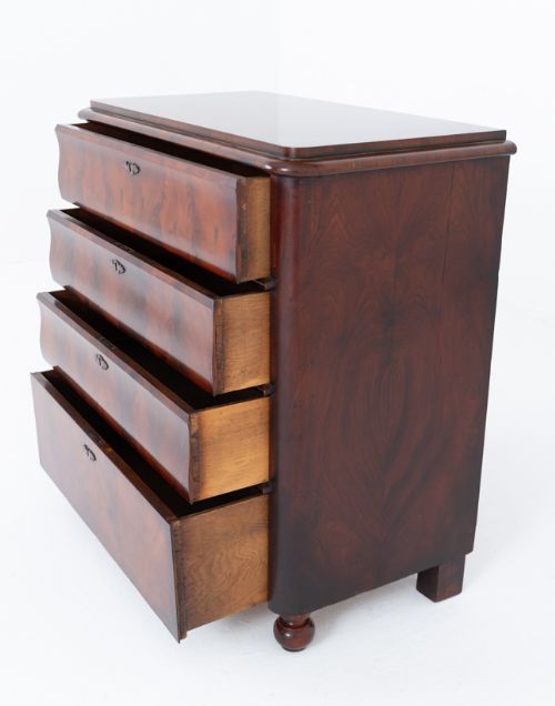 fig 1. An antique Biedermeier mahogany chest of drawers featuring four stacked drawers with book-matched flame veneer, dark keyhole escutcheons, and front bun feet.