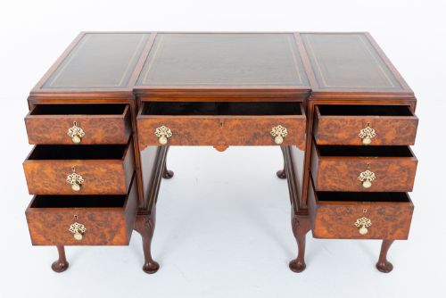 fig 1. A Queen Anne style burr walnut kneehole desk featuring an inset dark leather writing top, brass drop handles, and cabriole legs.