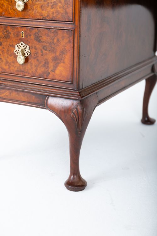 fig 2. A Queen Anne style burr walnut kneehole desk featuring an inset dark leather writing top, brass drop handles, and cabriole legs.