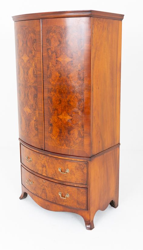 fig 1. A Regency Revival bow-fronted burr walnut wardrobe featuring double doors above two long drawers with brass drop handles.