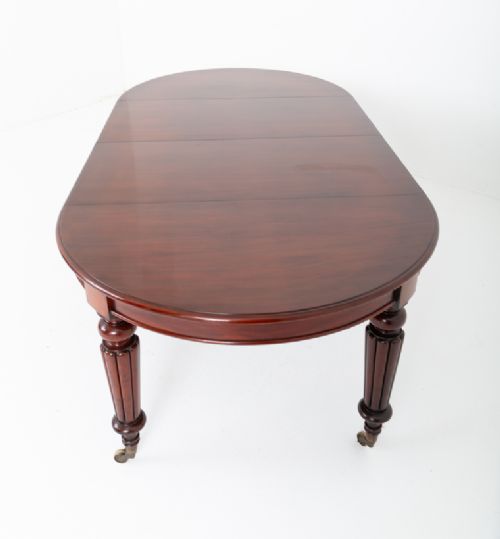 fig 1. An antique dark mahogany extending dining table with a polished top, central removable leaves, and fluted turned legs on brass castors.