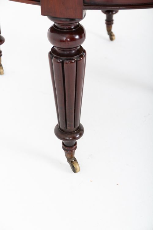 An antique dark mahogany extending dining table with a polished top, central removable leaves, and fluted turned legs on brass castors. View V