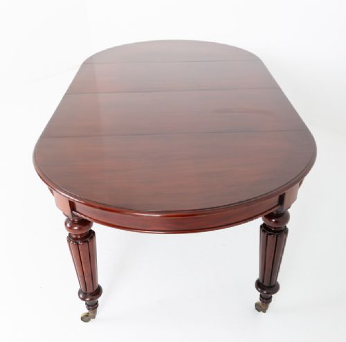 An antique dark mahogany extending dining table with a polished top, central removable leaves, and fluted turned legs on brass castors. View VII
