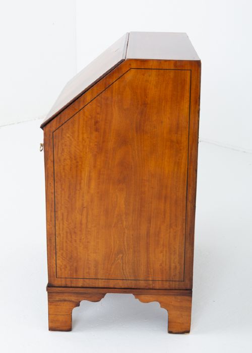 An antique mahogany writing bureau featuring a sloped fall-front flap over four graduated drawers with ornate brass handles and bracket feet. View IV