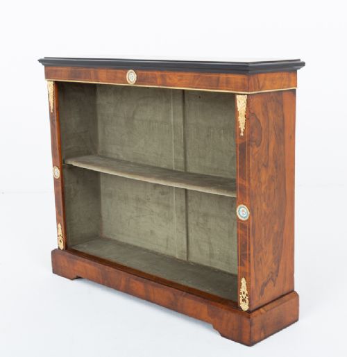 A Victorian burr walnut open bookcase featuring two open shelves, ebonised top trim, gilt brass mounts, and ceramic plaque details. View VII