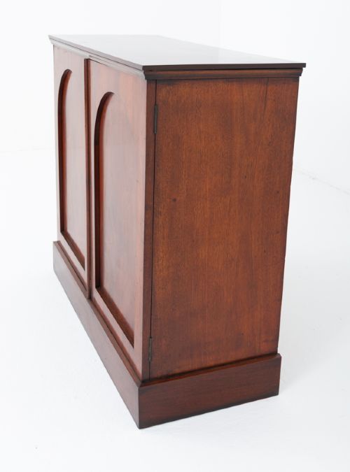 A Victorian mahogany side cabinet featuring two recessed arched panel doors and a solid plinth base. View VII