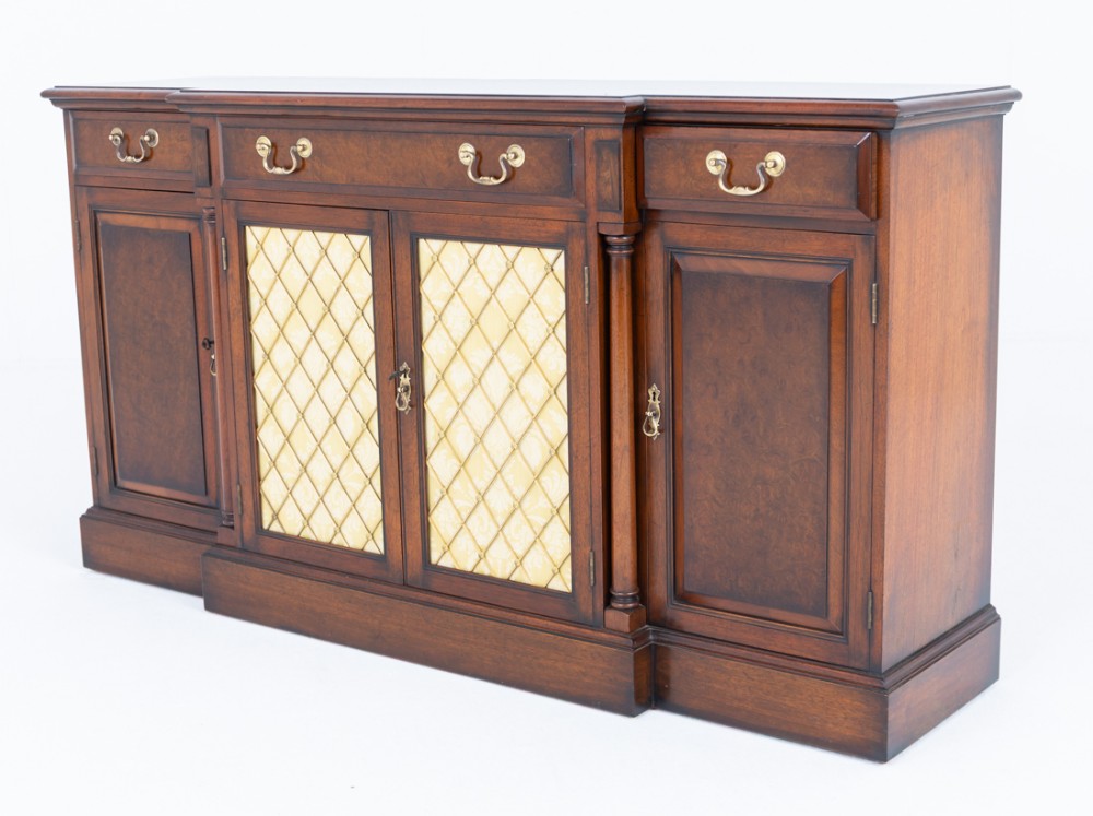 A Georgian Revival walnut breakfront sideboard featuring three upper drawers over four cupboard doors, with central brass lattice inserts, raised on a plinth base.