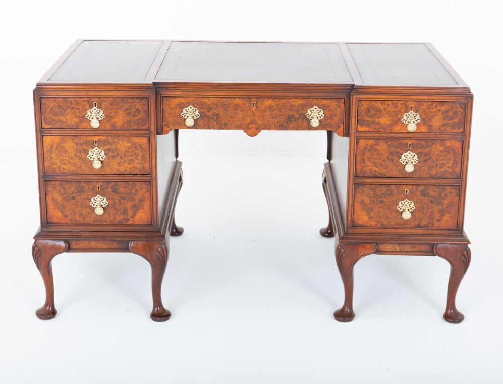 A Queen Anne style burr walnut kneehole desk featuring an inset dark leather writing top, brass drop handles, and cabriole legs. View IV