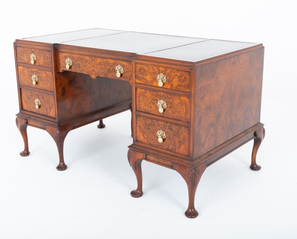 A Queen Anne style burr walnut kneehole desk featuring an inset dark leather writing top, brass drop handles, and cabriole legs. View VI
