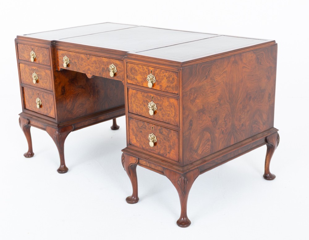 A Queen Anne style burr walnut kneehole desk featuring an inset dark leather writing top, brass drop handles, and cabriole legs.