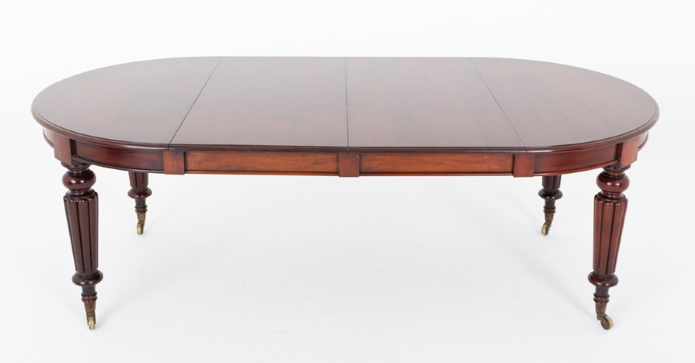 An antique dark mahogany extending dining table with a polished top, central removable leaves, and fluted turned legs on brass castors. View VI