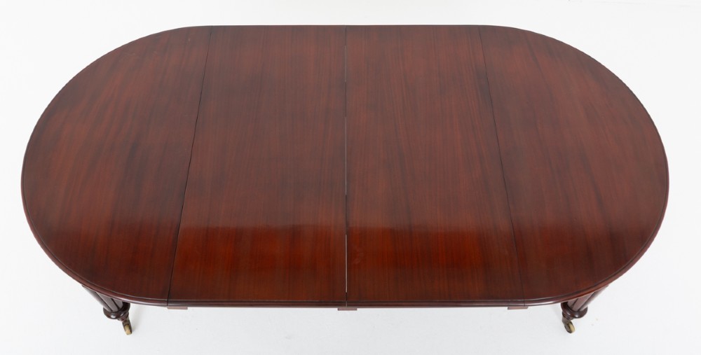 An antique dark mahogany extending dining table with a polished top, central removable leaves, and fluted turned legs on brass castors. View IX