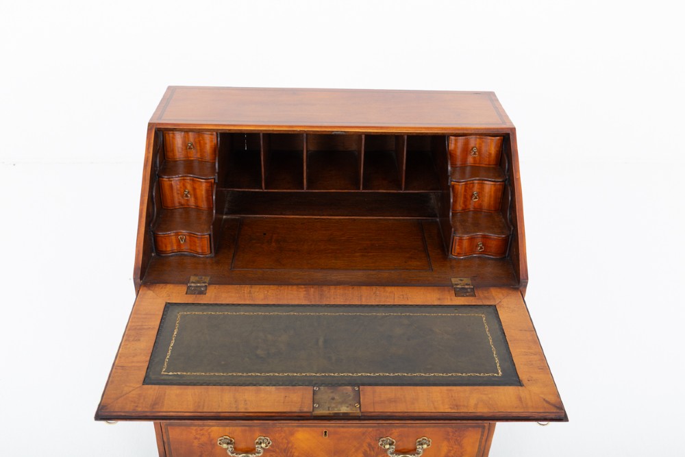 An antique mahogany writing bureau featuring a sloped fall-front flap over four graduated drawers with ornate brass handles and bracket feet. View II