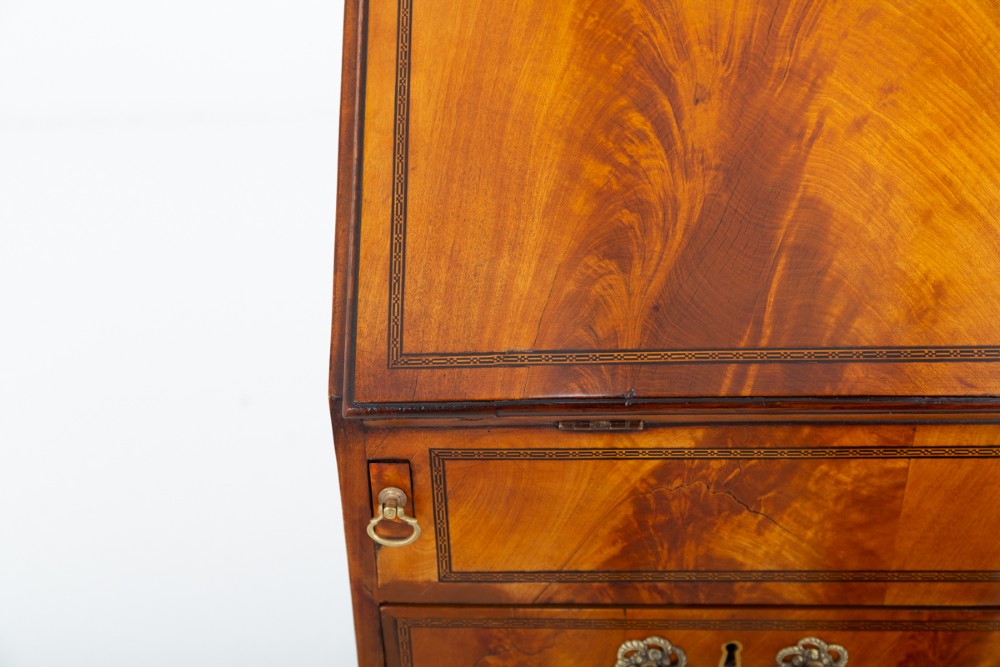 An antique mahogany writing bureau featuring a sloped fall-front flap over four graduated drawers with ornate brass handles and bracket feet. View VI