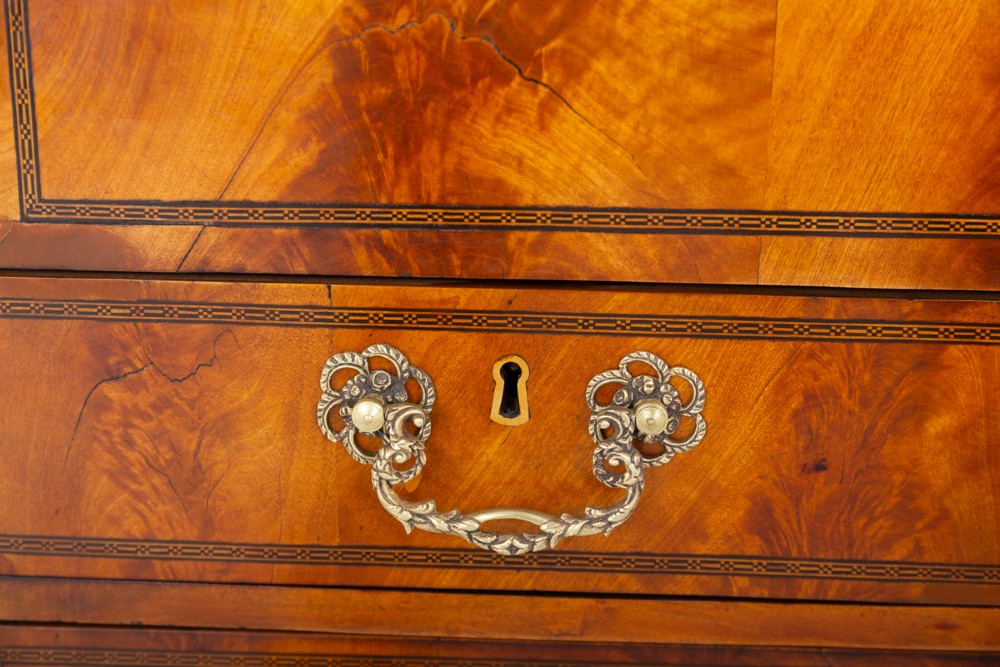 An antique mahogany writing bureau featuring a sloped fall-front flap over four graduated drawers with ornate brass handles and bracket feet. View IX