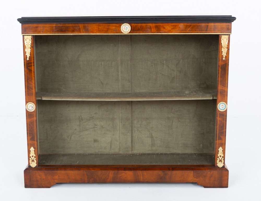 A Victorian burr walnut open bookcase featuring two open shelves, ebonised top trim, gilt brass mounts, and ceramic plaque details. View IV